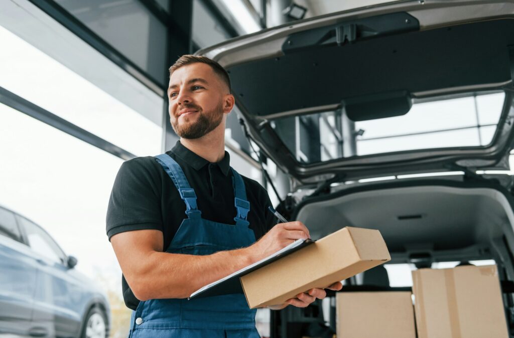 Portrait of delivery man in uniform that is indoors with car and with order